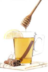 Transparent cup of tea with honey, cinnamon and lemon on white background.